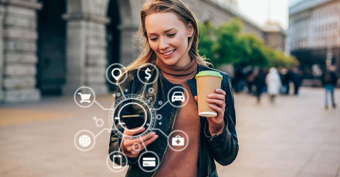 Woman holding a cup of coffee looks at different virtual representations of headless commerce trends extending from her mobile device.