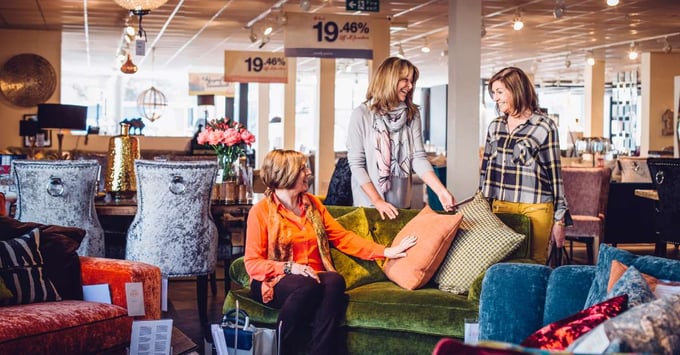 A group of women test out and sit on a couch inside of a home goods store.